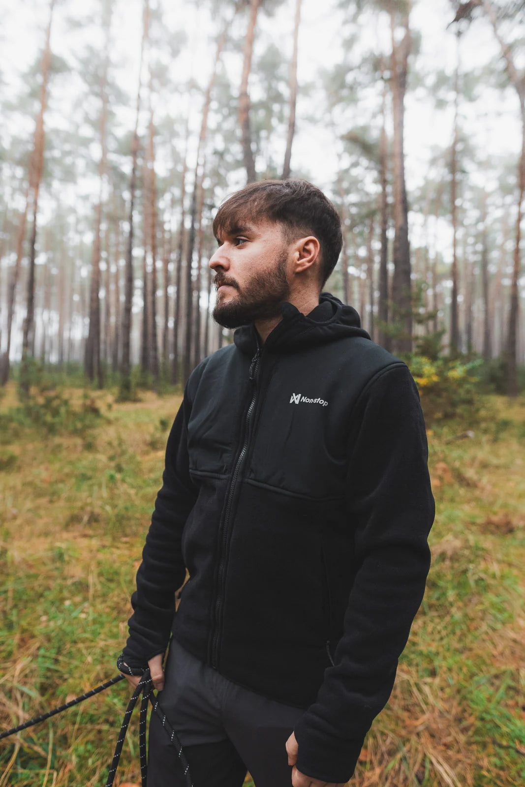 Man wearing a black jacket with a brand logo in a forest setting