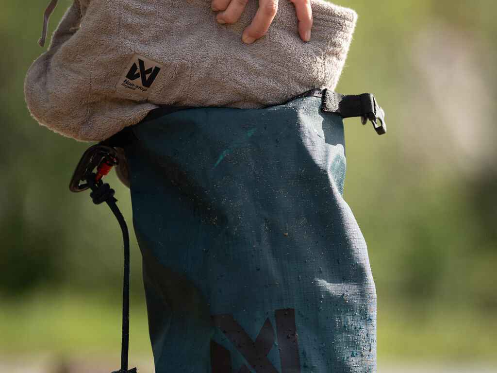 User placing towel into the Non-stop Dogwear Multiuse Bag, showcasing its spacious and waterproof interior for outdoor use.