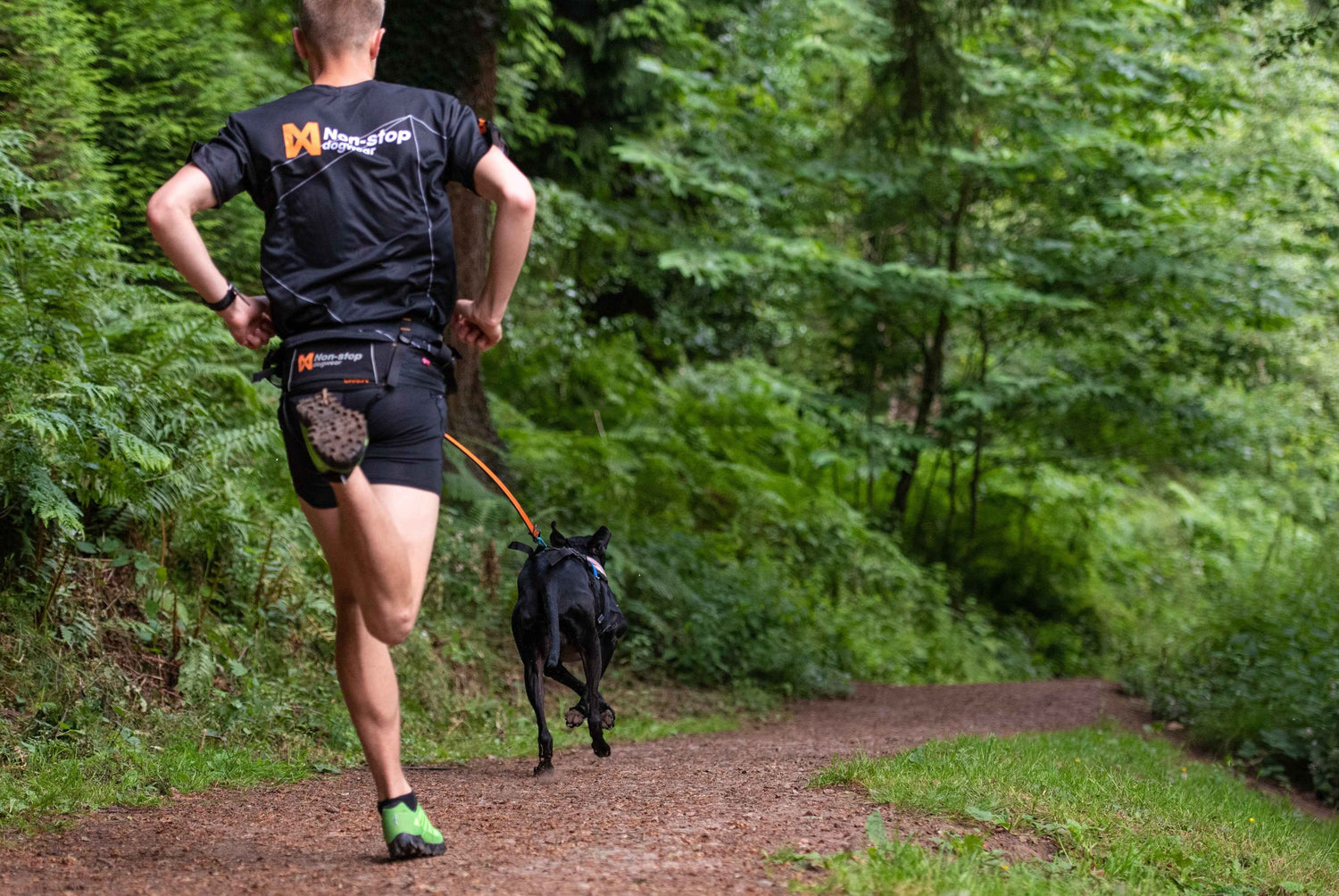 Man trail running with dog using Orange/Black Non-stop Dogwear Bungee Leash, designed for shock absorption and hands-free control.