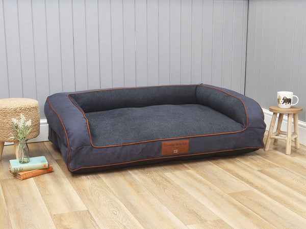 George Barclay Holbury Dog Sofa Bed - Moonlight, Blue pet bed with brown trim on a wooden floor against a gray wall.